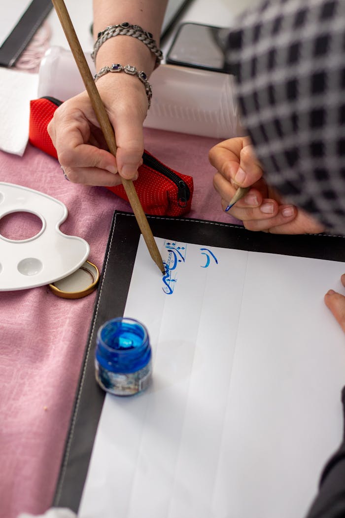 portfolio-01 Close-up of hands practicing calligraphy with blue ink and brush on paper.