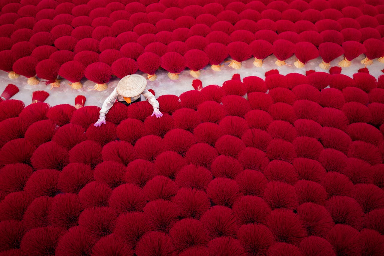 services-02 Aerial view of red incense sticks drying outdoors, worker in traditional hat.